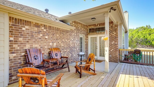Una terrazza in legno con poltrone Adirondack e un tavolo, un muro in mattoni e un portico coperto.
