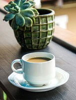 Una taza de café blanca sobre un plato, colocada sobre una superficie de madera.