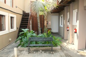 Un estrecho callejón con un banco de madera, una palmera y un extintor en la pared.