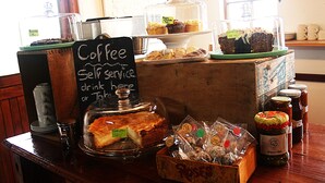 Een koffiehoek met een bordje, een vitrine met gebak en potten met toevoegingen.