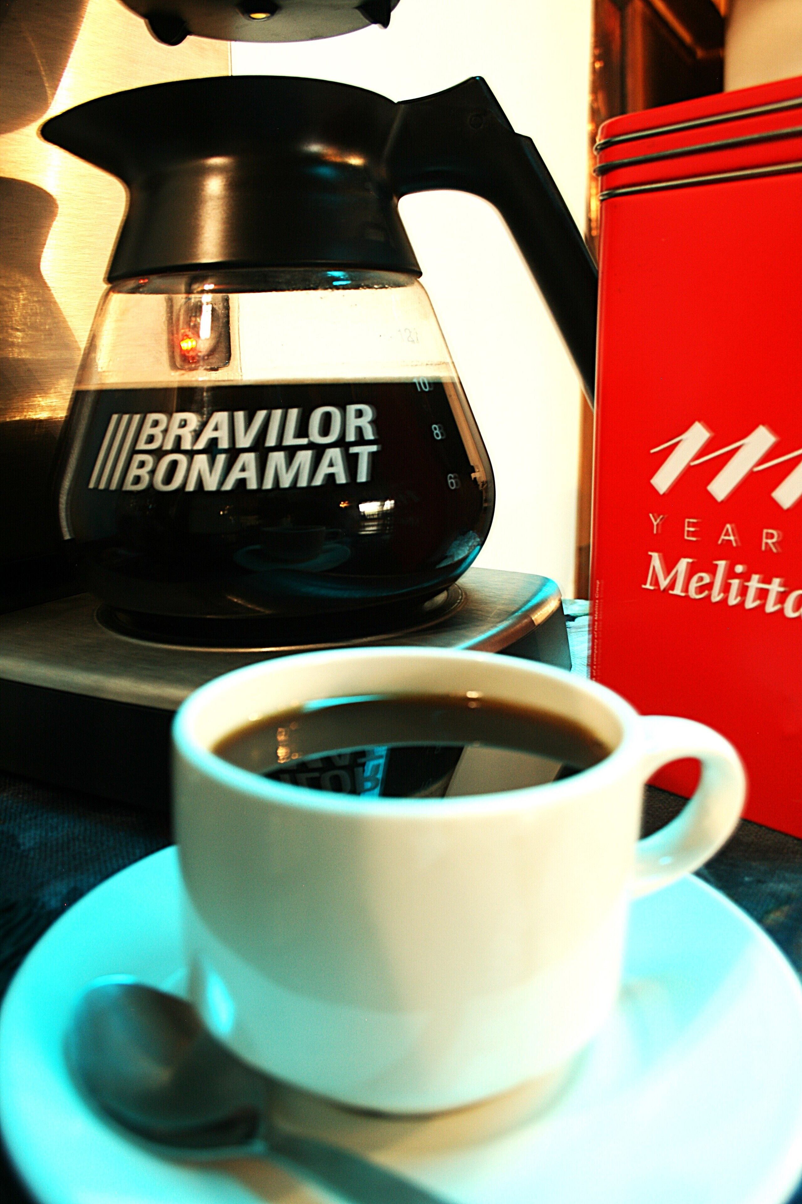 Una tassa de cafè sobre un plat, una cafetera i un llibre vermell.