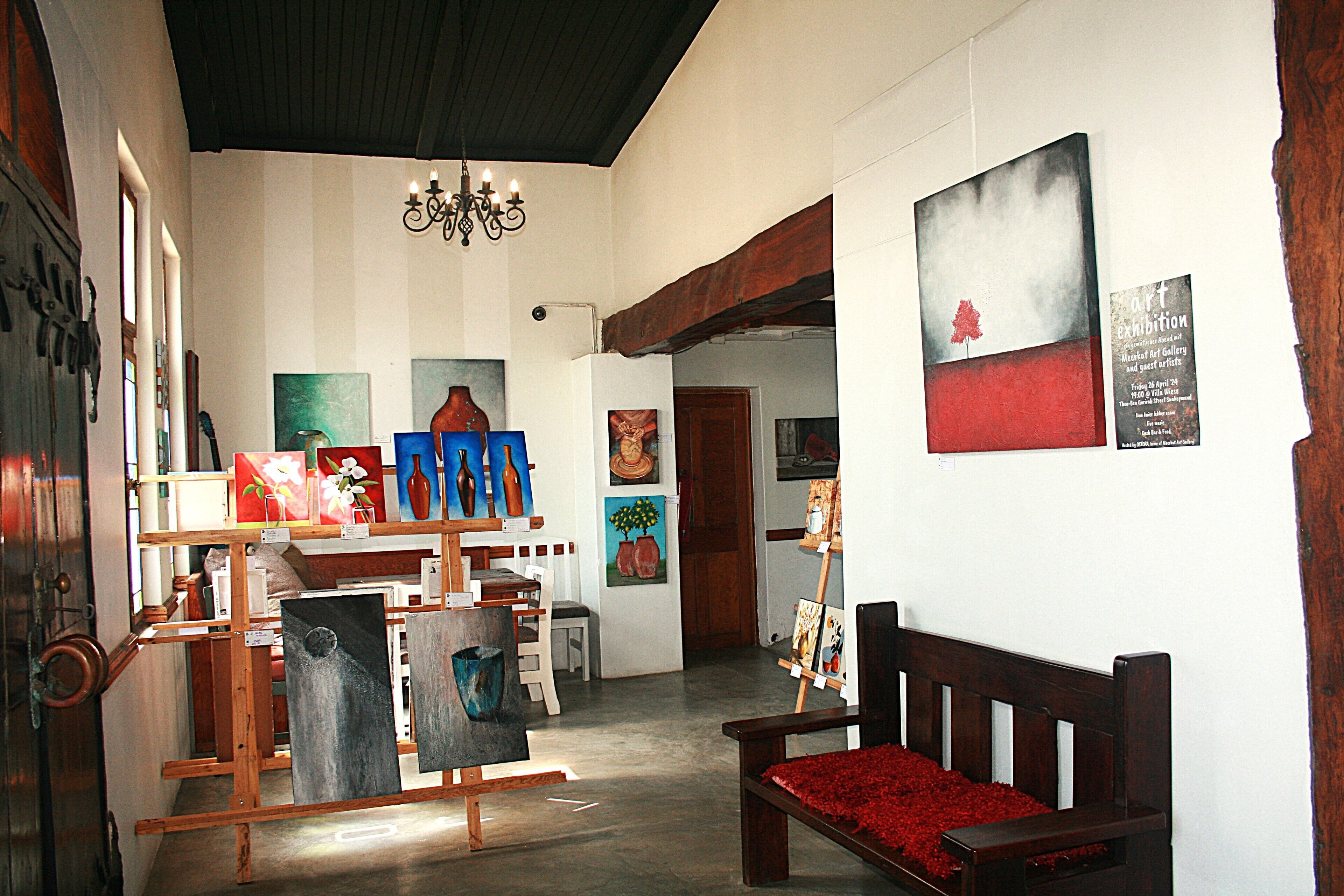 Une galerie d’art où sont exposées des peintures, un banc en bois et un lustre.