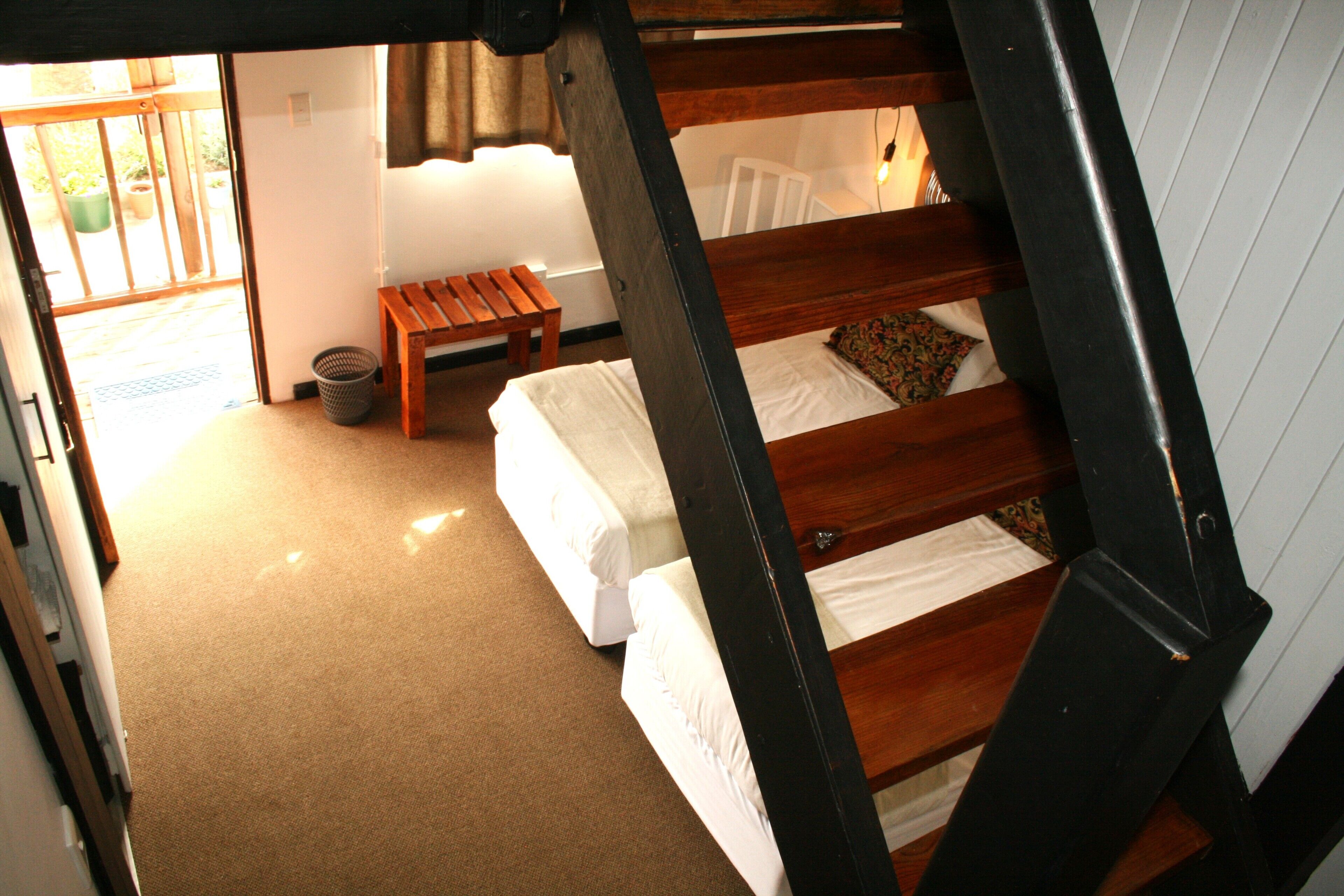 A room with a wooden staircase, a bench, and two beds with white linens.
