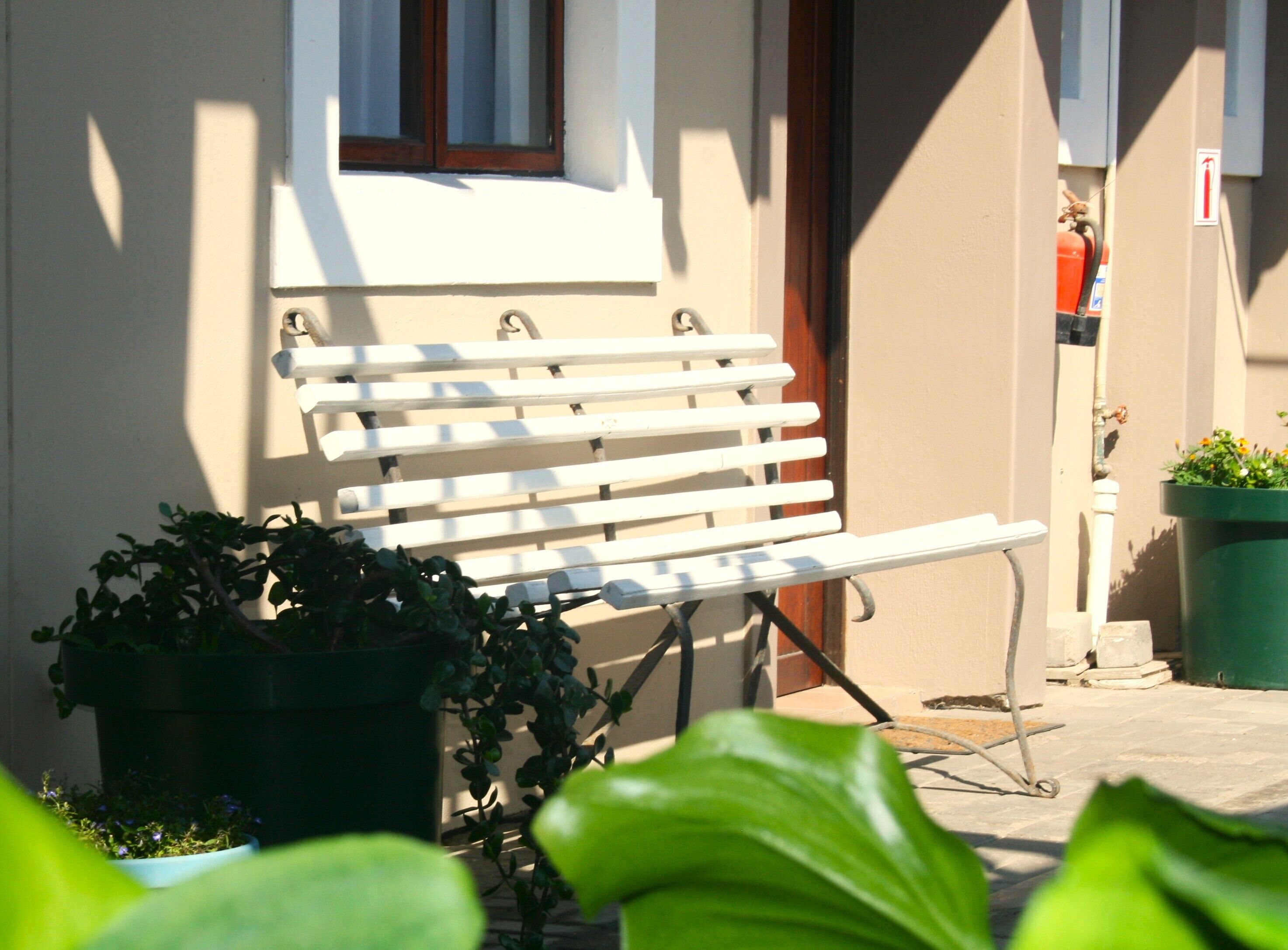 A white bench outside a building with a window and a potted plant nearby.