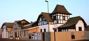 Edificio tradicional con un cartel que indica 'Villa Wiese' y 'Windhukersstr.'. Presenta una combinación de entramado de madera blanca y oscura, varios tejados a dos aguas y una farola.