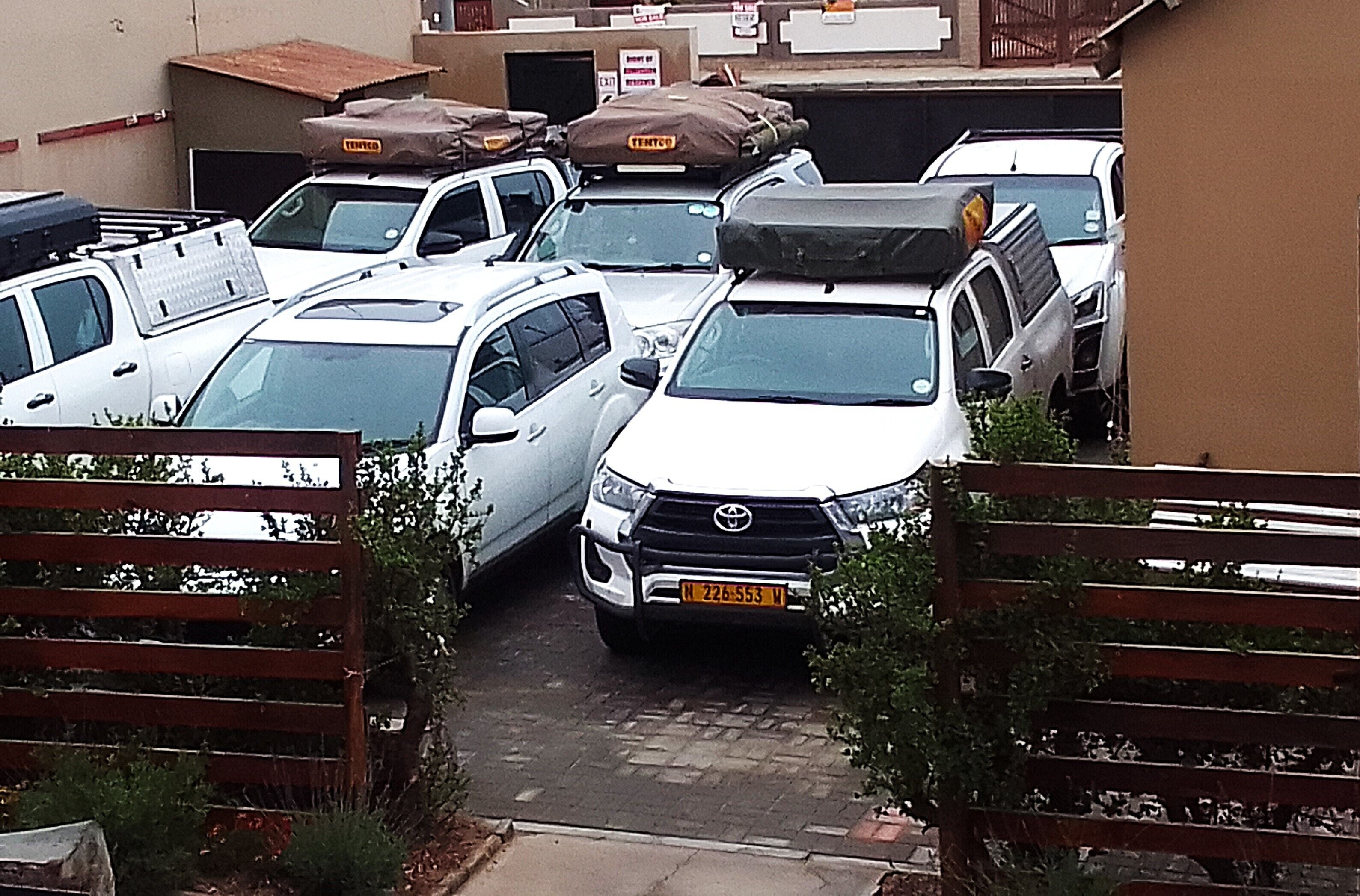 Un parking où sont stationnés plusieurs véhicules blancs, dont certains ont des bagages sur le toit.