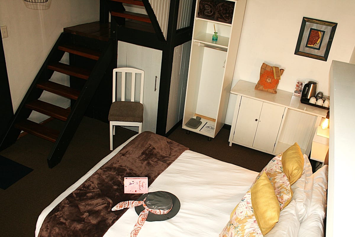 Un dormitorio con cama, una silla, un escritorio, un espejo, un estante y una escalera.