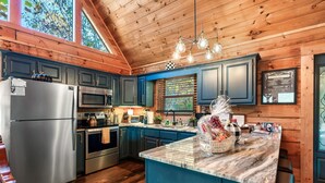 A modern kitchen with wooden walls, stainless steel appliances, and a marble island. - Smoky Mountain Ridge Retreat / Panoramic Views • Hot Tub • Game Room & Balconies (Gatlinburg)