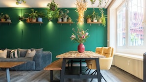 En moderne stue med en grøn væg, træmøbler og flere krukker med planter.