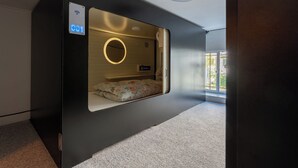 Et kompakt, moderne værelse med en indbygget seng, et lille natbord og et kontrolpanel på væggen.