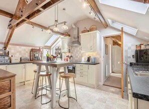 A spacious kitchen with high ceilings, exposed beams, and a central island with stools. - Ocean View Luxury top Floor Harbourside Apartment (Lowestoft)