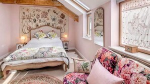 Een slaapkamer met een houten bed, een bloemen hoofdbord, een grote spiegel en uitzicht op een stadsbeeld door een raam.