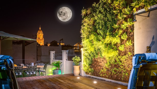 A rooftop patio with wooden flooring, outdoor seating, and a view of a moonlit night sky with a building in the background. - Solaga - Sagrado Corazon (Málaga)