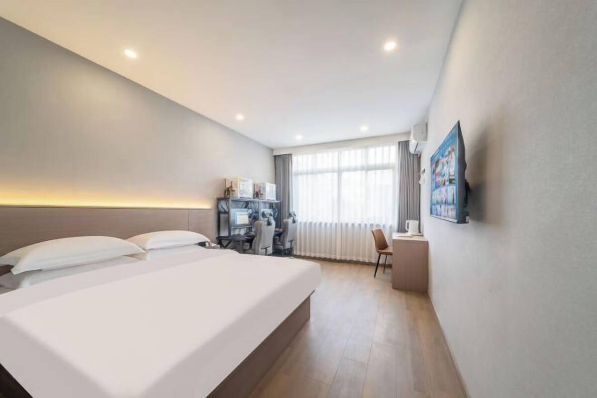 A hotel room with a bed, desk, chair, and a large window.