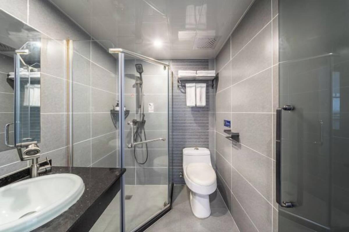 A modern bathroom with a glass shower enclosure, a white toilet, and a sink with a dark countertop.