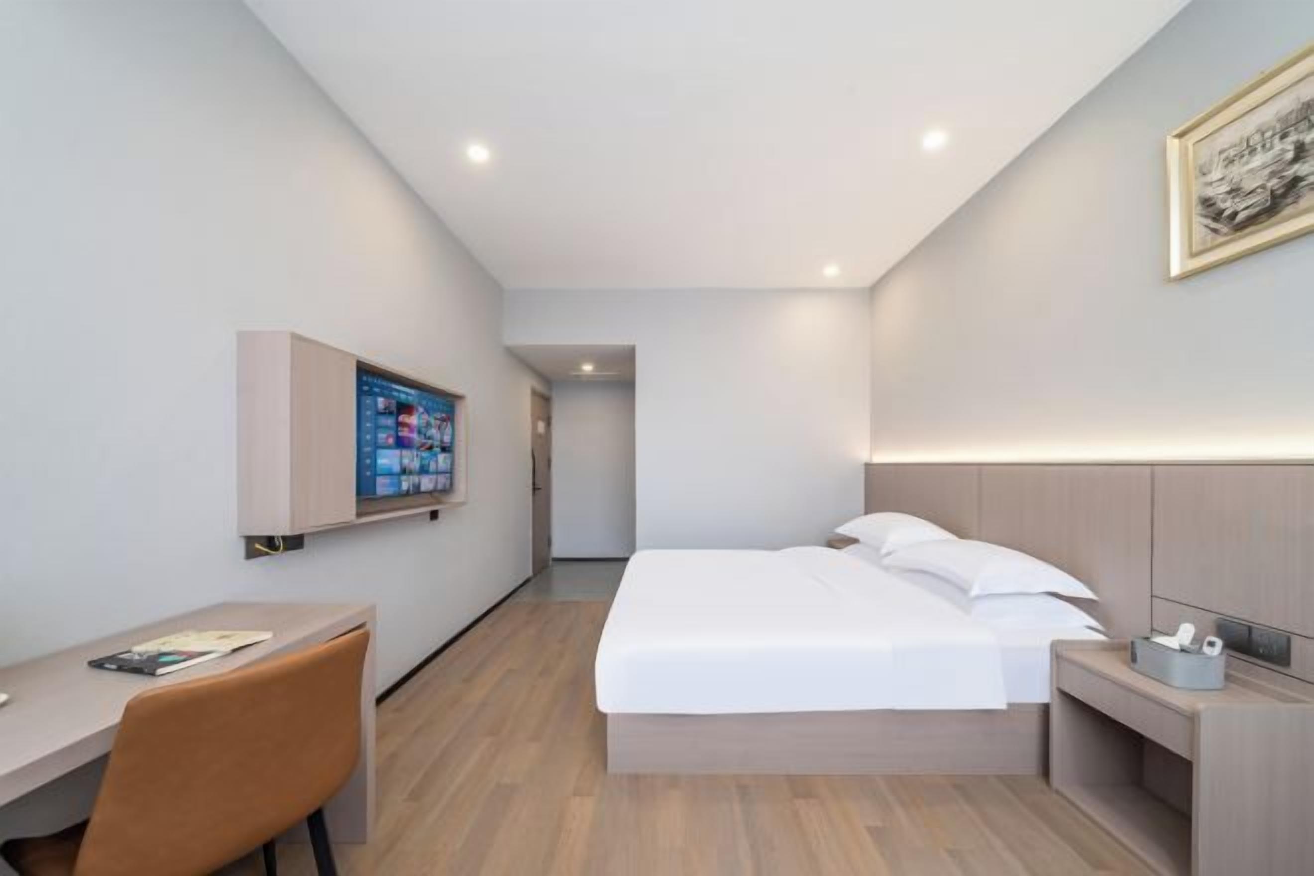 A modern hotel room with a bed, a desk, and a TV mounted on the wall.