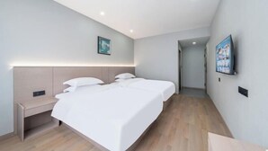 Quarto de hotel moderno com uma cama grande, mesas de cabeceira, uma TV de tela plana na parede e um corredor que leva a outro quarto.