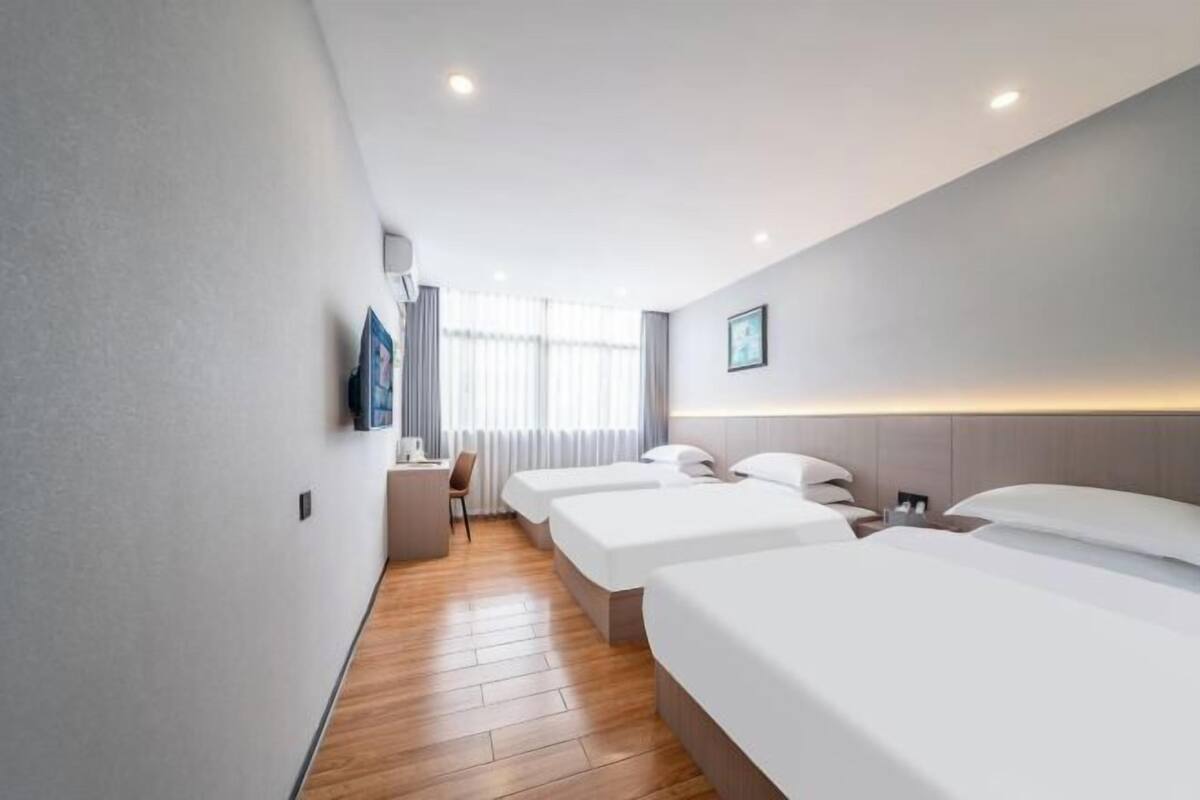 A hotel room with three beds, a desk, and a chair.