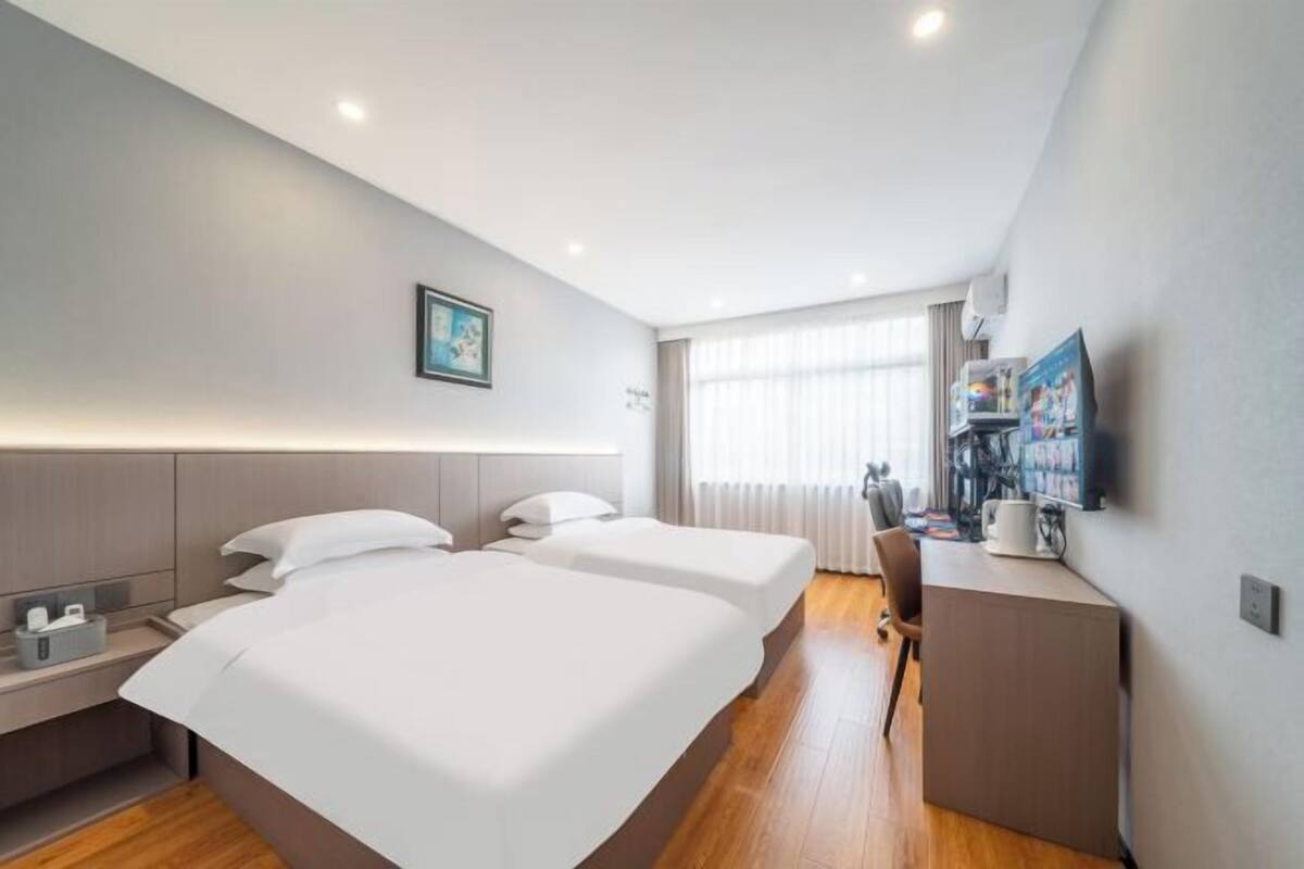 A hotel room with two beds, a desk, a chair, a TV, and a window with curtains.