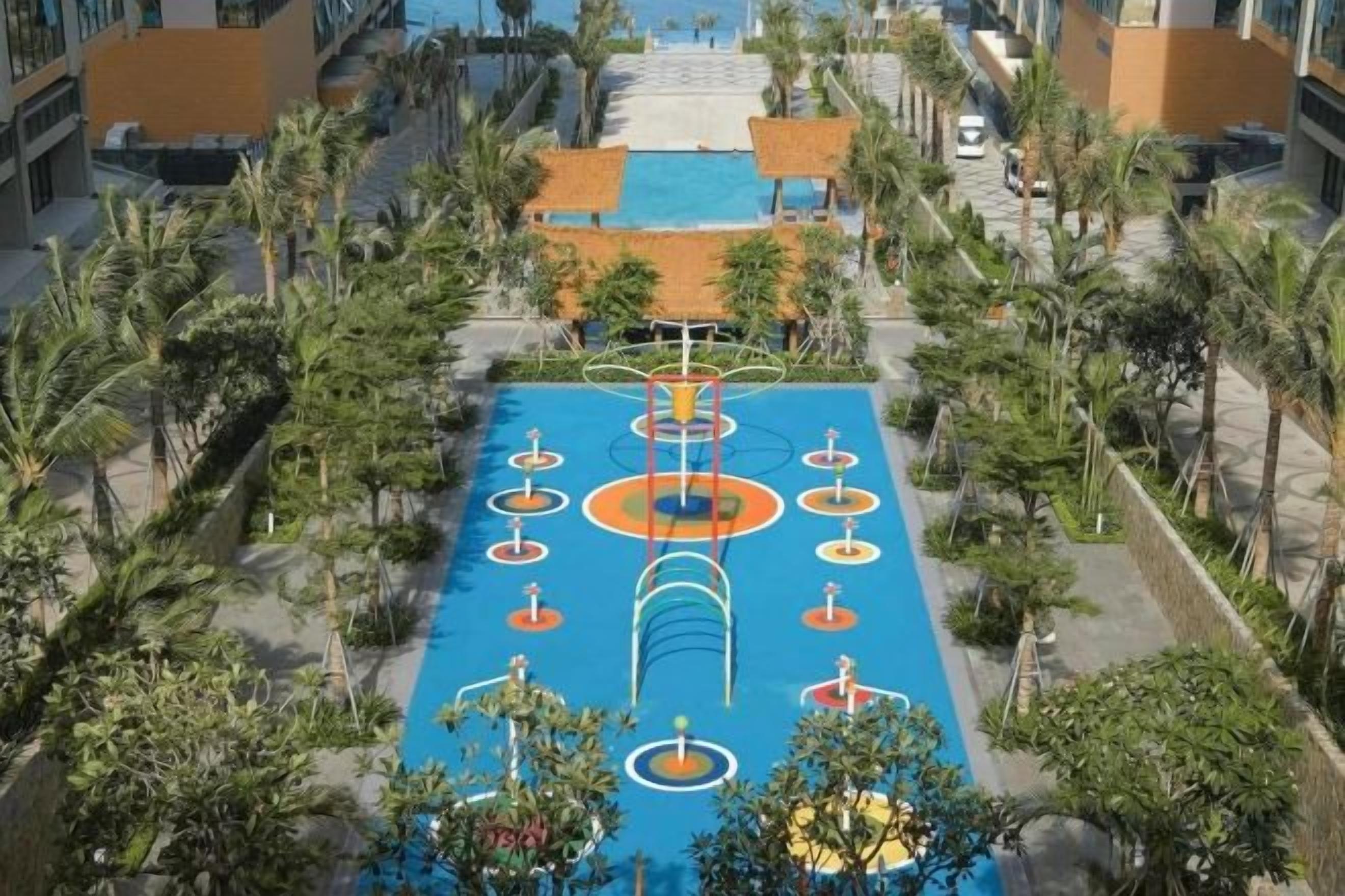 An aerial view of a resort with a pool area, palm trees, and a clear sky.
