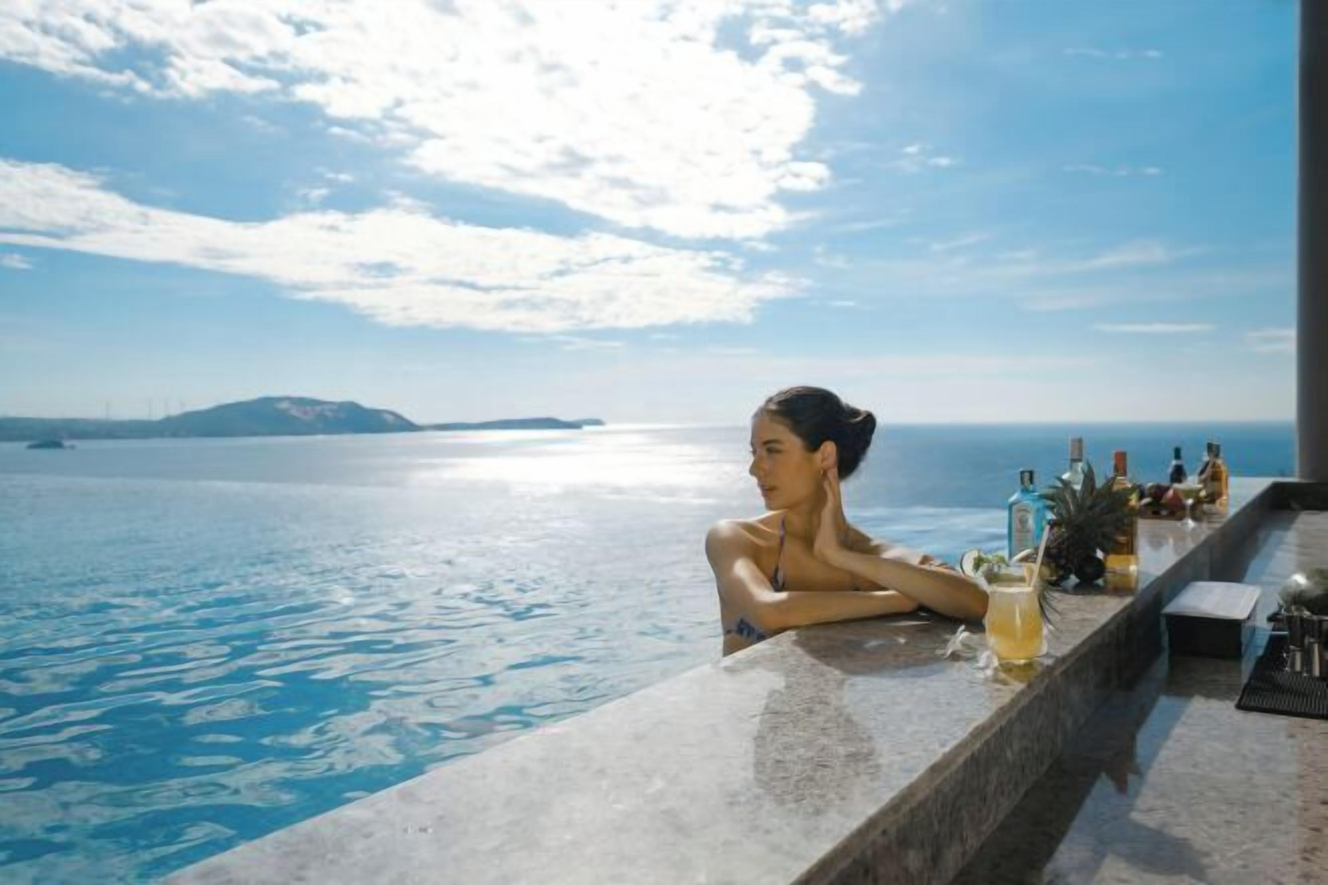 Una persona descansando junto a una piscina con vista al mar y a islas en la distancia.