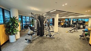Ein modernes Fitnessstudio mit verschiedenen Trainingsgeräten, großen Fenstern und einer Decke mit integriertem Licht.