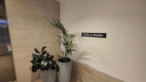 Ein modernes Interieur mit einem Schild, das einen Pool- und Sauna-Bereich anzeigt, zwei Blumentöpfen und einem wandmontierten Aufzug.