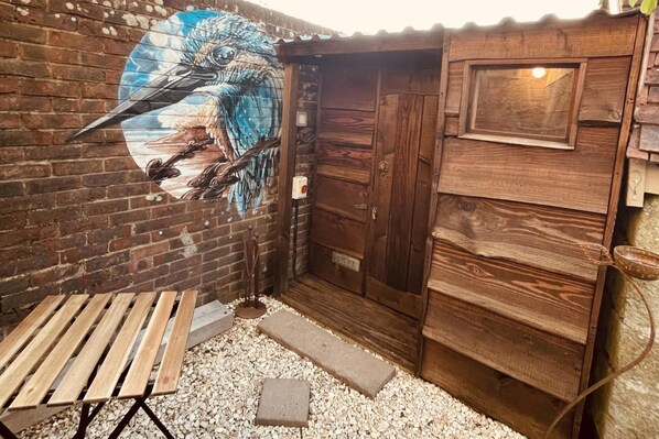 A rustic wooden door with a window, a wooden bench, and a mural of a bird on a brick wall.