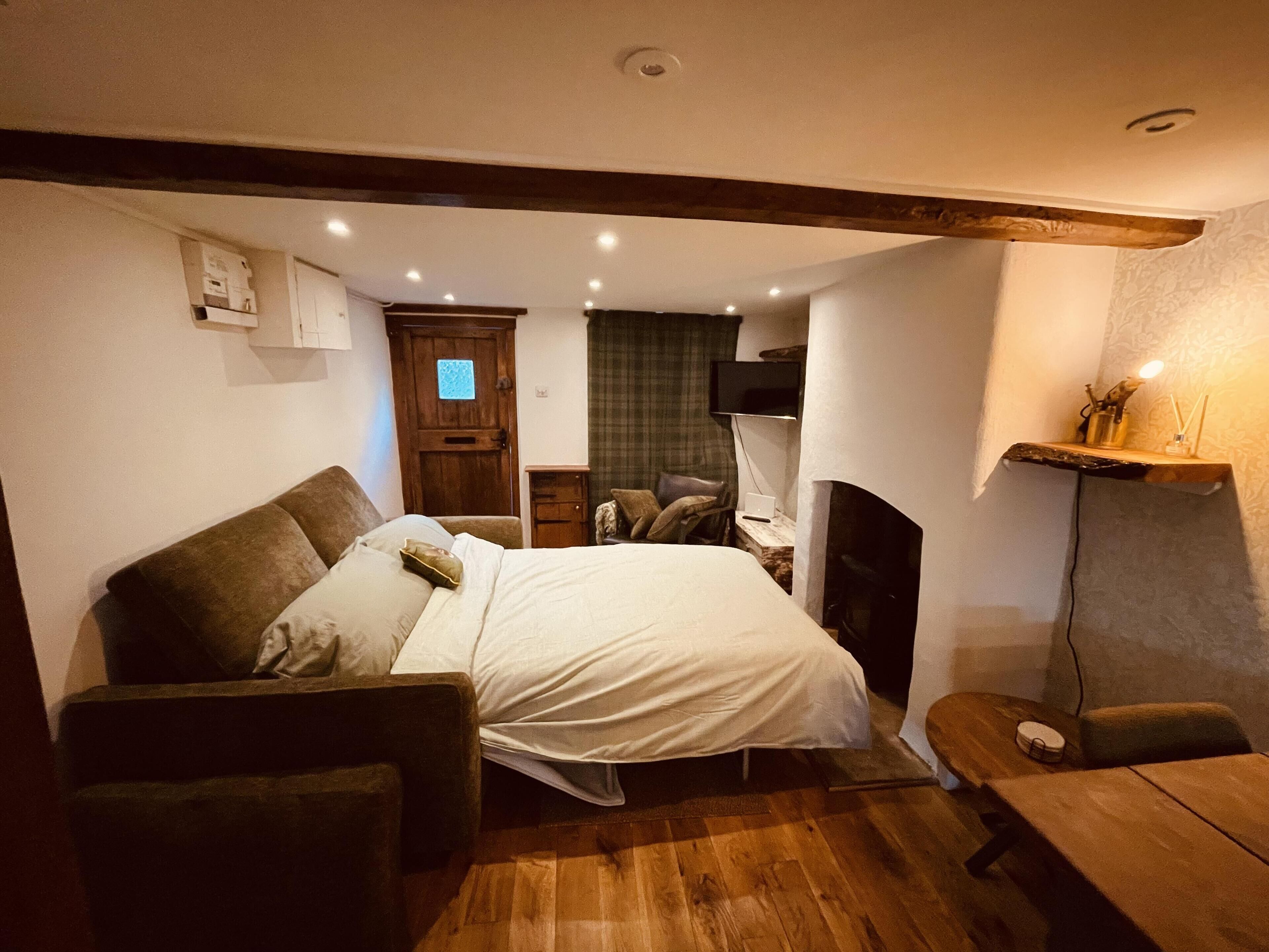A cozy bedroom with a bed, a wooden floor, a small desk, a chair, a TV, and a fireplace.