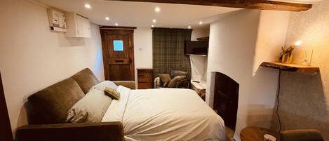 A cozy bedroom with a bed, a wooden floor, a small desk, a chair, a TV, and a fireplace.