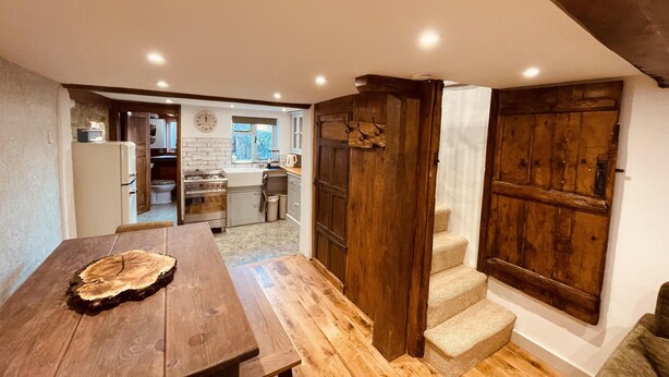 A kitchen with a wooden table, a sink, and a stove. There is a wooden door and a staircase leading to another room.