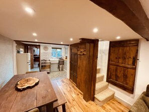 A kitchen with a wooden table, a sink, and a stove. There is a wooden door and a staircase leading to another room.