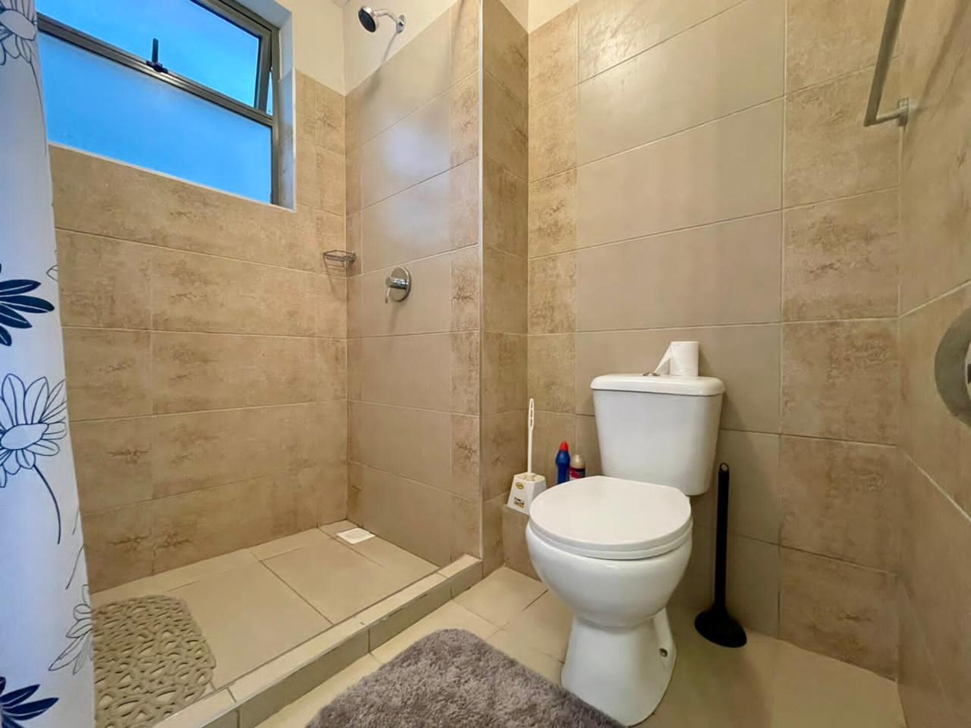 A bathroom with a toilet, shower, and a small window.
