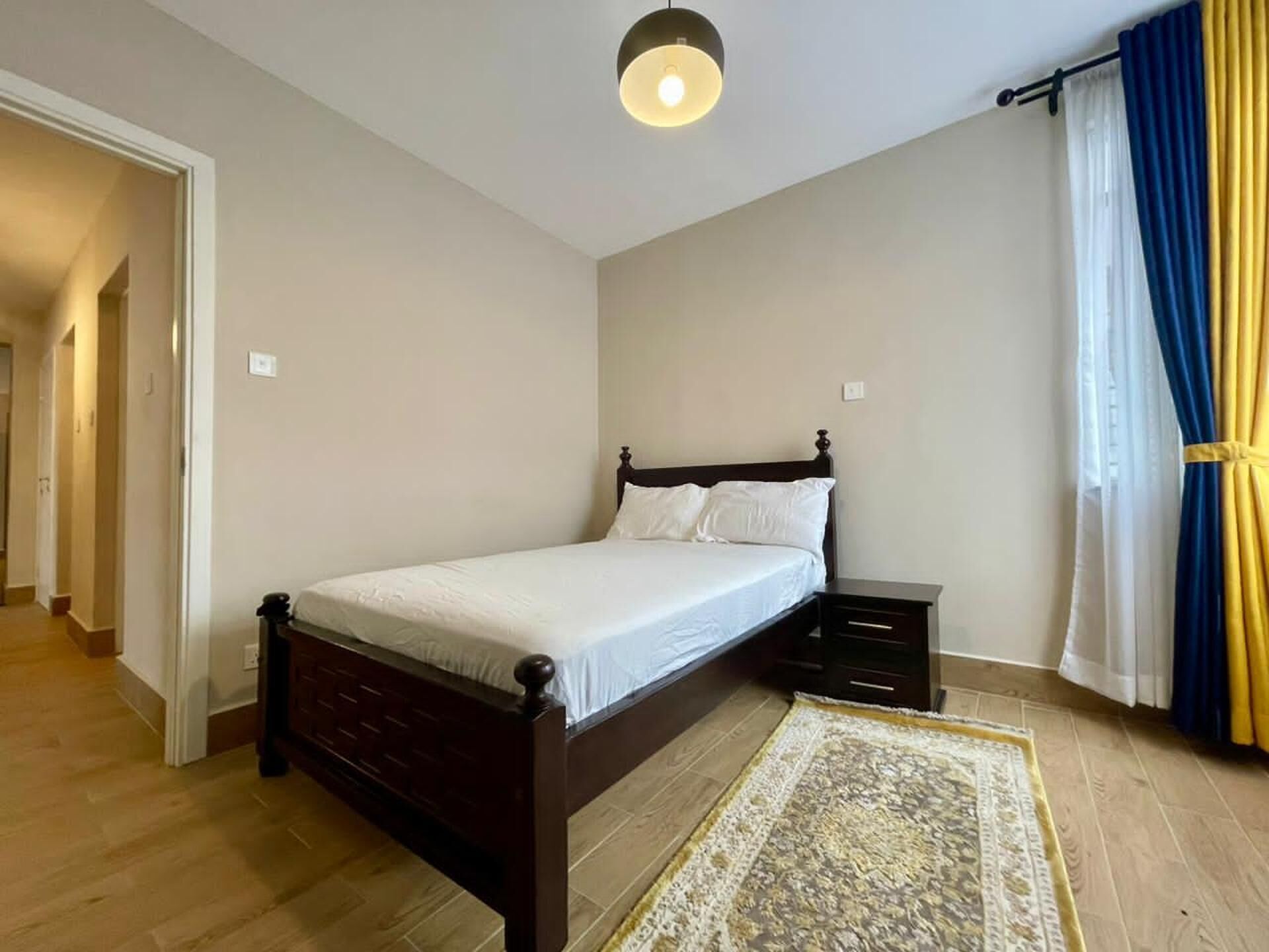 A bedroom with a wooden bed, bedside tables, a rug, and a ceiling light.