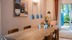 A dining area with a wooden table, chairs, a vase with flowers, and a painting on the wall. - Anubis_relaxed&stay! Stylish short-term accommodation in leafy Hamburg-Niendorf (Hamburg)