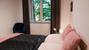 A bedroom with a bed, a chair, a window with curtains, and a nightstand with a lamp and a flower. - Anubis_relaxed&stay! Stylish short-term accommodation in leafy Hamburg-Niendorf (Hamburg)