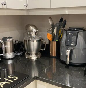 A kitchen counter with a mixer, a coffee maker, and a container with utensils. - Luxury Central Hale Living (Altrincham)