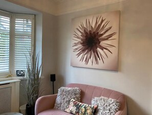 A living room with a pink sofa, two grey pillows, a large abstract painting, a potted plant, and a radiator. - Luxury Central Hale Living (Altrincham)