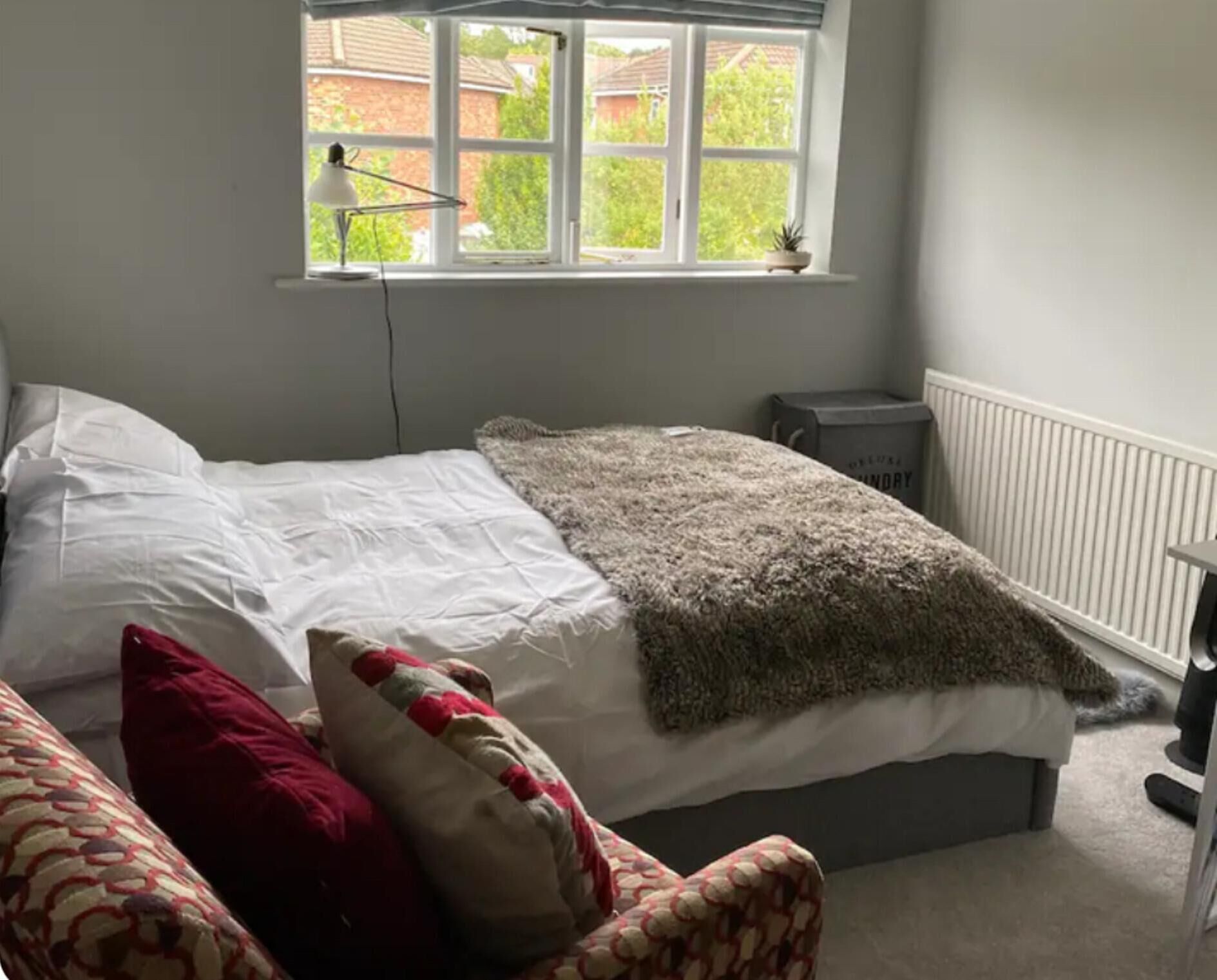 Un dormitorio con una cama, una ventana, un radiador y una silla.