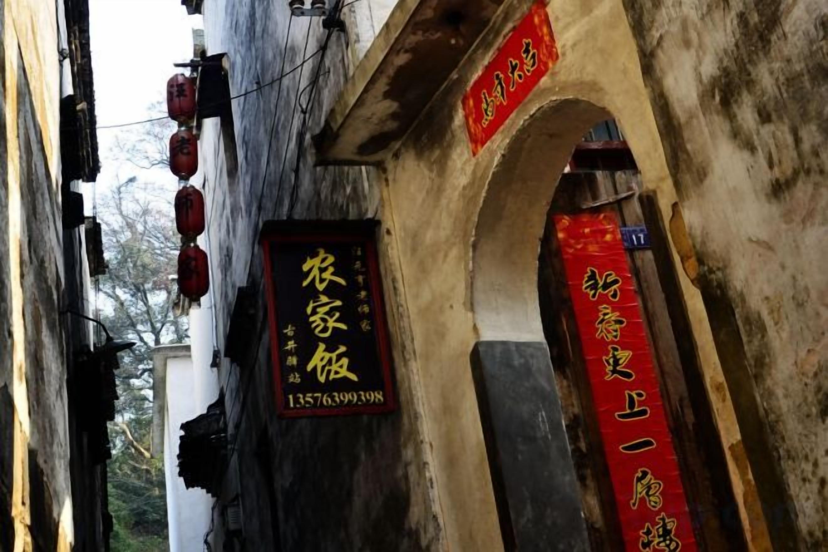A narrow alleyway with traditional architecture, including an arched doorway and hanging red lanterns.