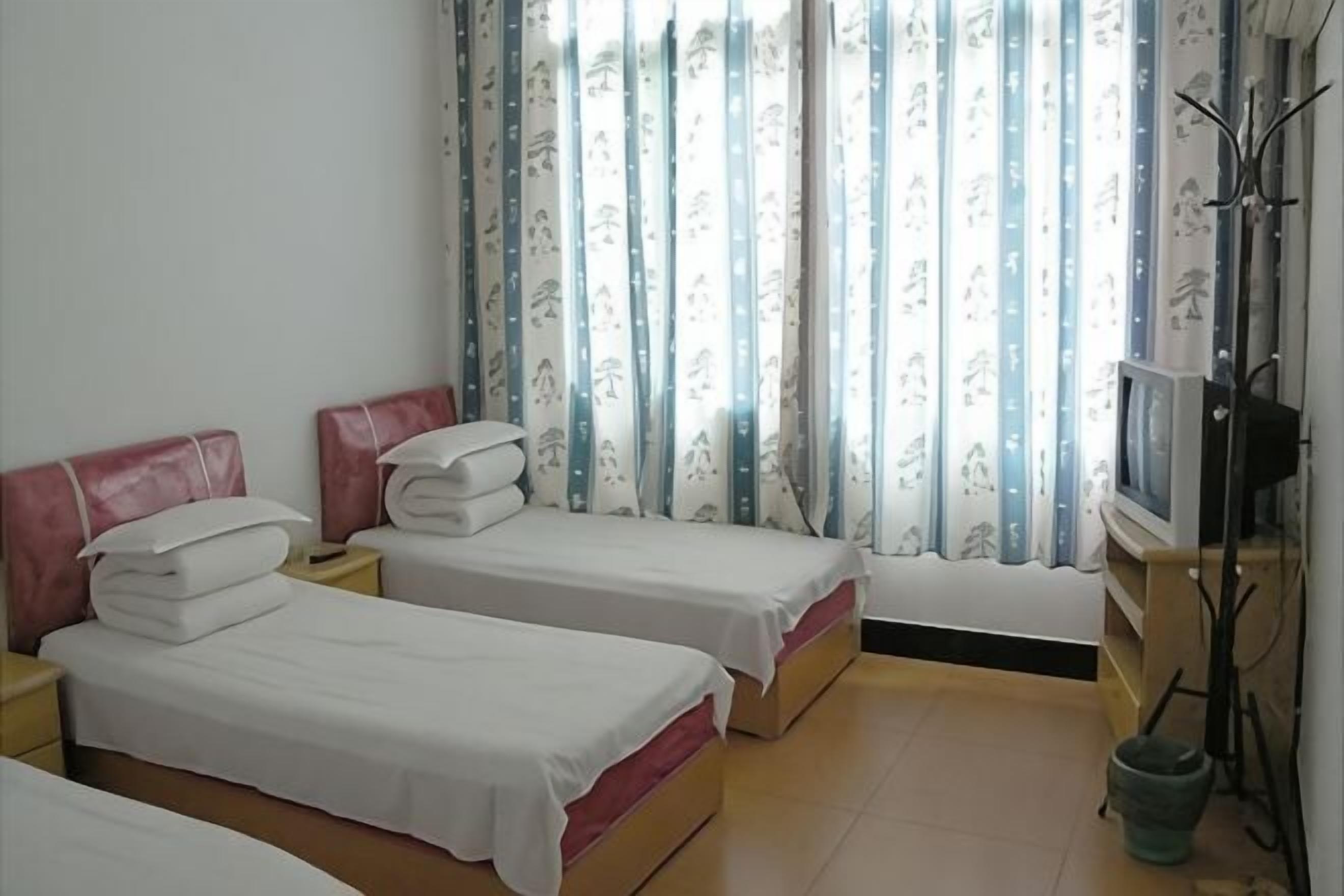 A room with two beds, a television, and a window with curtains.