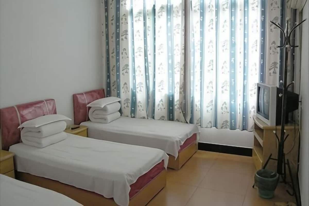 A room with two beds, a television, and a window with curtains.