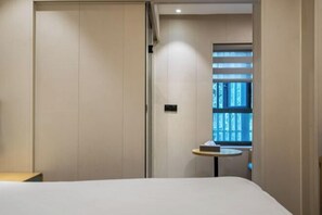 Una habitación de hotel con una cama, una mesita, una ventana con persianas y una puerta.