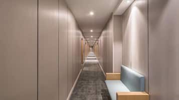 Un long couloir étroit d’hôtel, avec un banc et une table de chevet sur le côté droit.