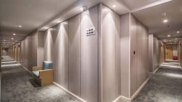 A hotel corridor with a long row of rooms, a sign indicating a smoking area, and a seating area with chairs.