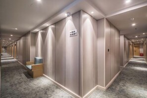 Een hotelgang met een lange rij kamers, een bordje dat een rookruimte aangeeft, en een zithoek met stoelen.