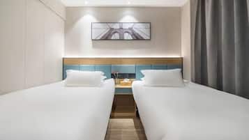 Habitación de hotel con dos camas individuales, un cabecero de madera, una mesita con un florero y un cuadro en la pared.