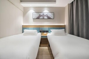 Habitación de hotel con dos camas individuales, un cabecero de madera, una mesita con un florero y un cuadro en la pared.