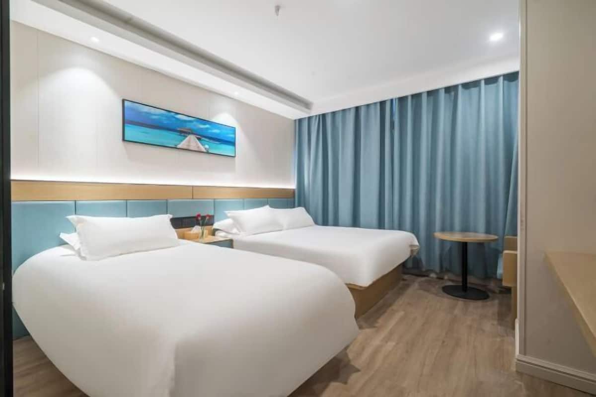 Ein Hotelzimmer mit zwei Betten, einem kleinen Tisch, einem Bild an der Wand und Meerblick durch das Fenster.