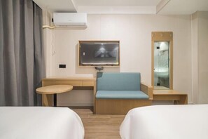Habitación de hotel con dos camas, un escritorio, una silla, una mesita, un televisor y zona de ducha.